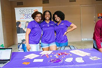 three students promoting 'sister 2 sister' club at a booth